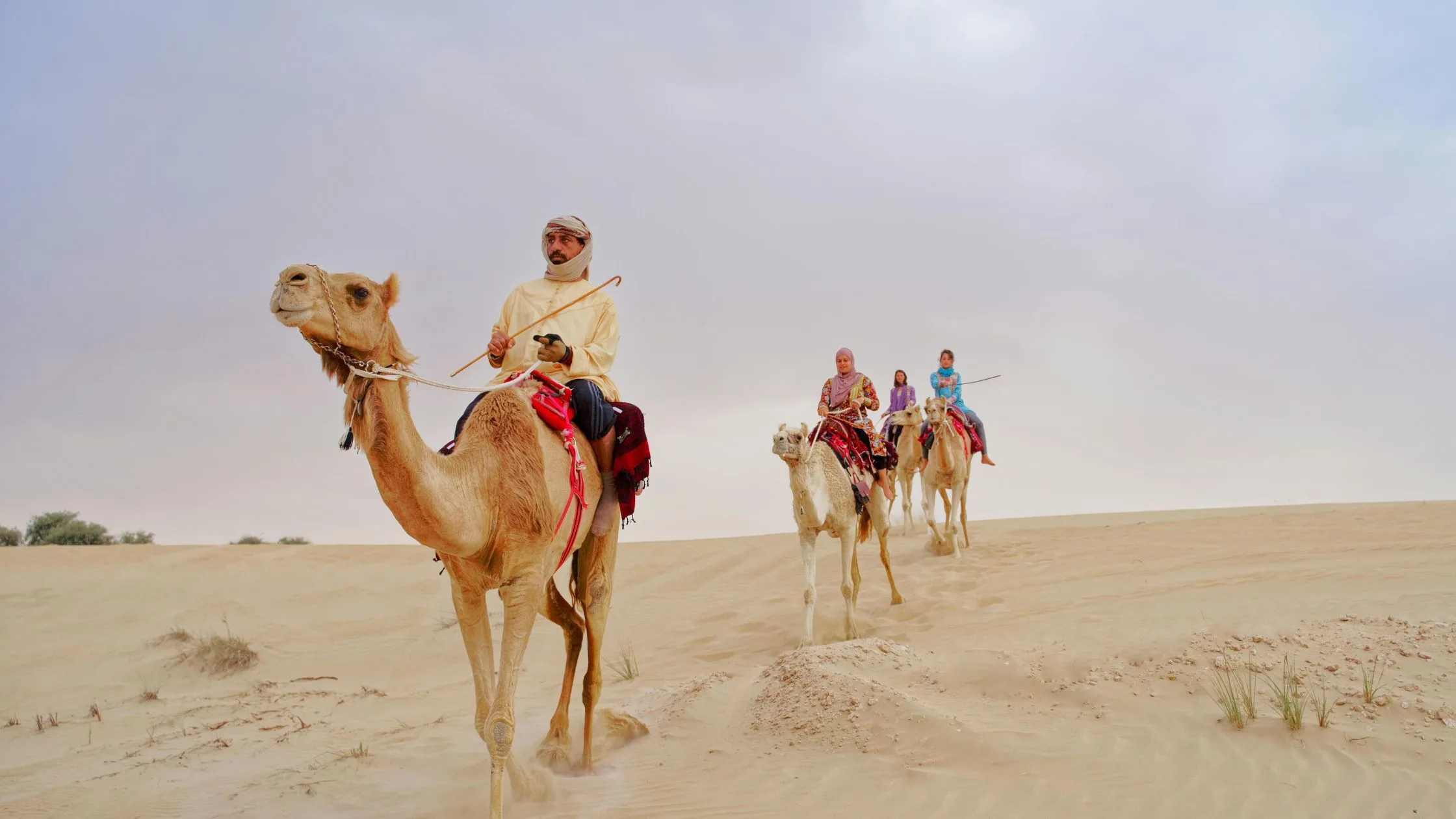 Tourists enjoying a camel ride during a desert safari in Abu Dhabi, exploring golden sand dunes under a cloudy sky.