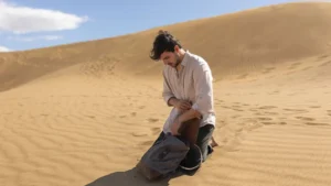 Traveler searching inside a backpack while sitting on desert sand dunes in Abu Dhabi